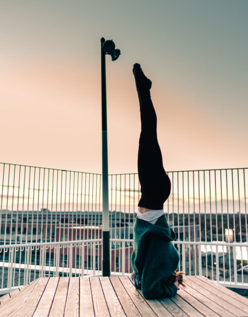 Camilla practicing yoga on a rooftop at sunrise. She's doing a headstand and working on fulfillment in her yoga practice