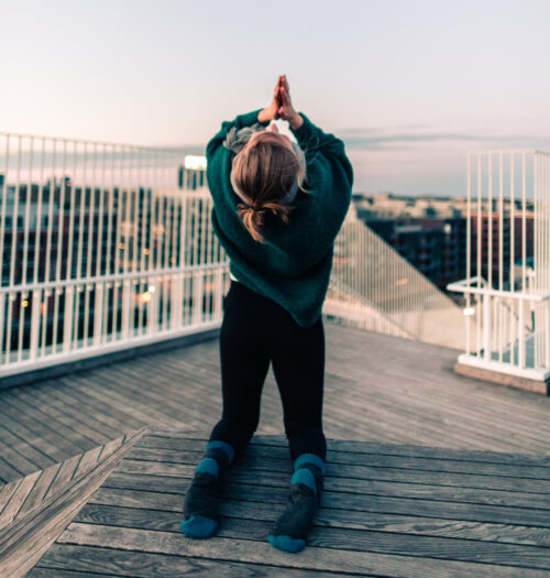 Camilla practicing yoga on a rooftop at sunrise. She's doing a camel pose and working on fulfillment in her yoga practice