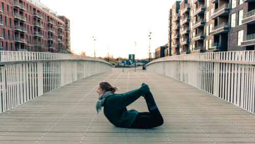 Camilla practicing yoga on a rooftop at sunrise. She's doing a bow pose and working on fulfillment in her yoga practice