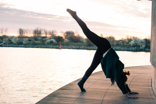 Camilla practicing yoga overlooking the water at sunrise. She's doing a 3 legged downward dog and working on fulfillment in her yoga practice