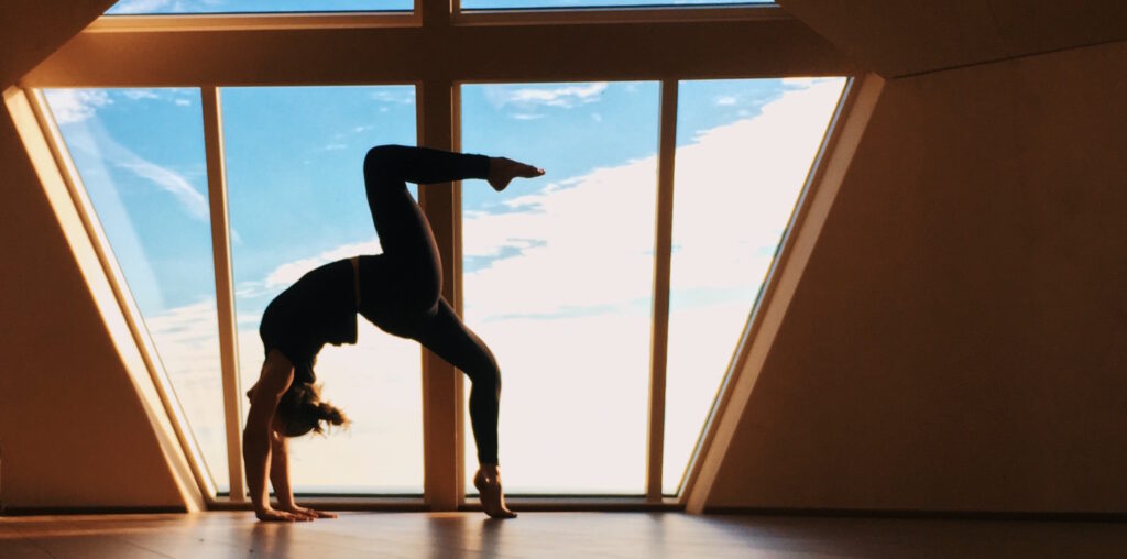 Backbend silhouette in front of big window overlooking the ocean