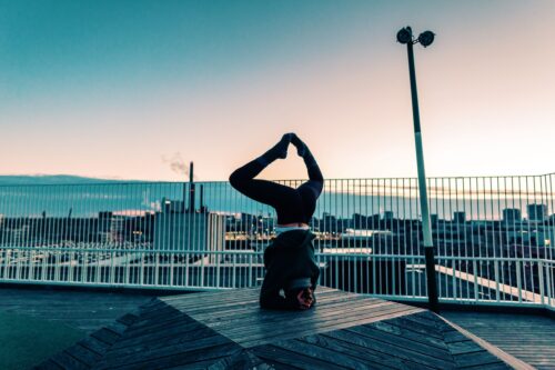 Camilla practicing yoga on a rooftop at sunrise. She's doing a headstand and working on fulfillment in her yoga practice