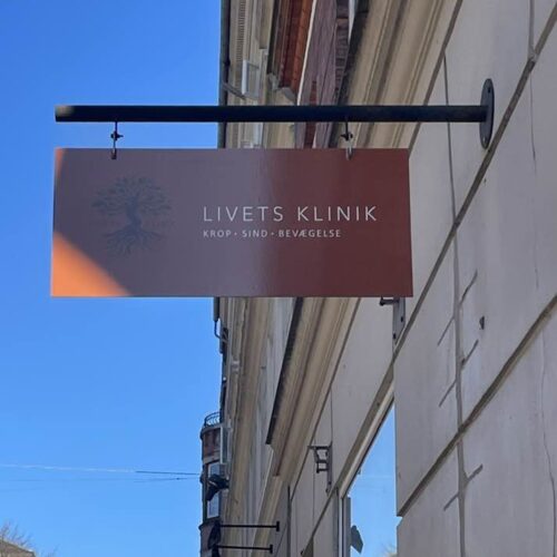 Livets Klinik skilt i brændt orange farve, der hænger ude på gaden med kontrasten af blå himmel i baggrunden