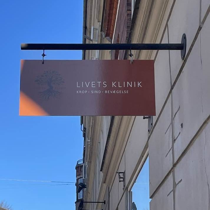 Livets Klinik skilt i brændt orange farve, der hænger ude på gaden med kontrasten af blå himmel i baggrunden