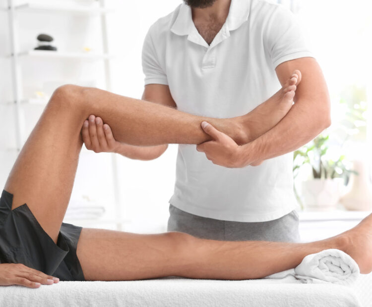 En klient ligger på en osteopatisk briks og osteopaten holder hans ben og undersøger knæets muskler, led og lednære strukturer såsom ledbånd. Dette foregår på en osteopati klinik i København.